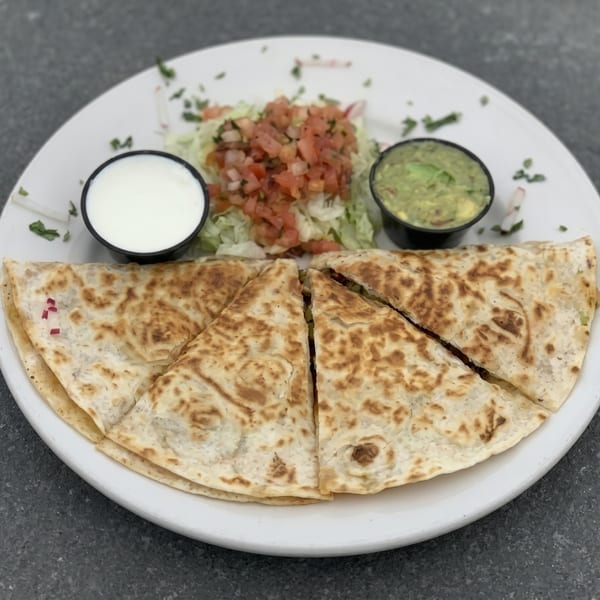 Quesadilla wedges with sides of sour cream, guacamole, and pico de gallo on a white plate.