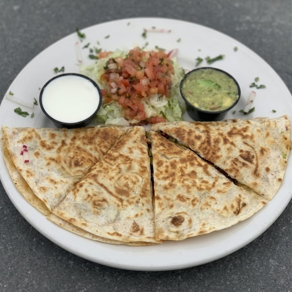 Quesadilla wedges with sides of sour cream, guacamole, and pico de gallo on a white plate.