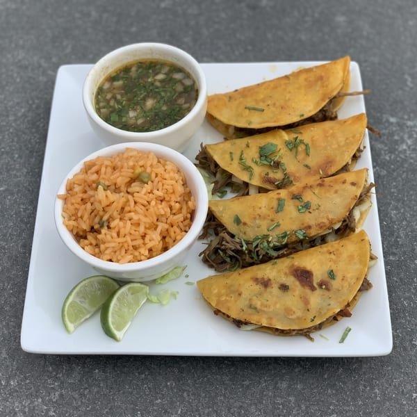 Four golden-brown birria tacos with cilantro, a side of rice, consommé, and lime wedges.