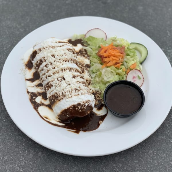 A burrito covered in mole sauce and cheese, served with a side salad and a cup of sauce.