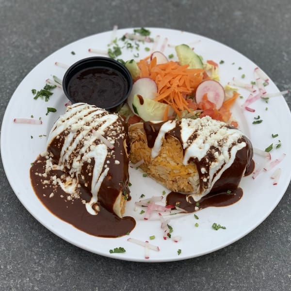 Two burritos covered in mole sauce, crema, and cotija cheese, with a side salad.