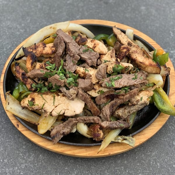 Sizzling fajitas with grilled chicken, steak, onions, and green peppers on a cast iron platter.